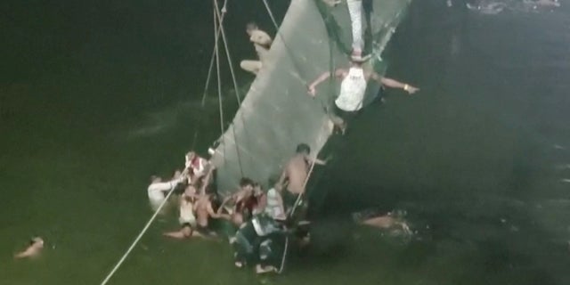 People cling on to the collapsed suspension bridge in Morbi, India October 30, 2022 in this screen grab obtained from a video. (ANI/ Handout via REUTERS)