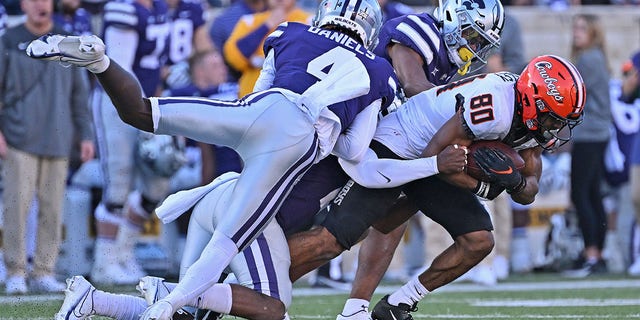 MANHATTAN, KS - OCTOBER 29:  Cornerback Omar Daniels #4 and safety Josh Hayes #1 of the Kansas State Wildcats tackle wide receiver Brennan Presley #80 of the Oklahoma State Cowboys during the second half at Bill Snyder Family Football Stadium on October 29, 2022 in Manhattan, Kansas.