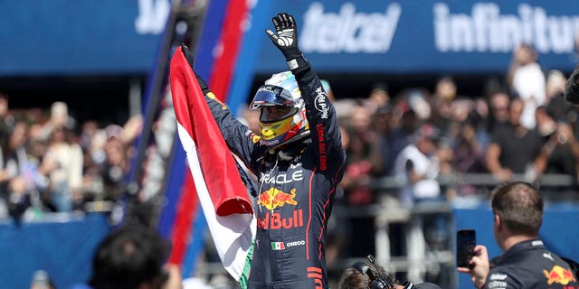 Mexican Formula One Red Bull driver Sergio "Checo" Perez waves at fans while holding a Mexican national flag after an exhibition race through the streets of Guadalajara, Mexico, Tuesday, Oct. 25, 2022. 