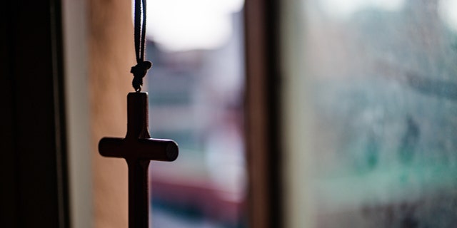 Cross necklace hanging in front of a window