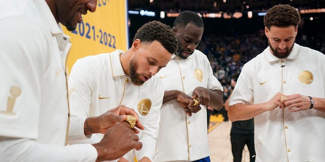 The Golden State Warriors' Andre Iguodala, Stephen Curry, Draymond Green and Klay Thompson look at their 2021-2022 NBA championship rings before the team's game against the Los Angeles Lakers in San Francisco Oct. 18, 2022.