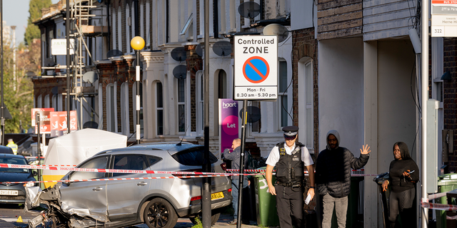 A police officer speaks with local residents the morning after two males were killed in a double-shooting on Railton Road, between Herne Hill and Brixton, on Oct. 31 2022, in London. Wreckage has been spread across the road after Met police were called at about 7:50 p.m. GMT the night before, after reports of gunshots between a car and moped were heard by witnesses.