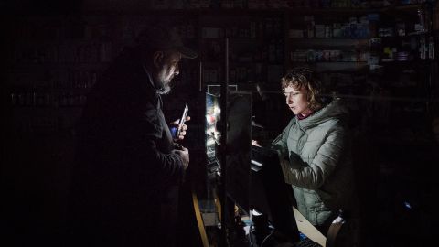 In a pharmacy in Lviv, a man uses the light on his phone to  help the pharmacist find products, amid rolling blackouts, on November 16.
