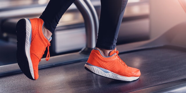 Comfortable sports shoes for running in the gym. Jogging shoes for running on a treadmill. Safety when performing exercises on cardio in sports shoes. Orange sports sneakers on the treadmill